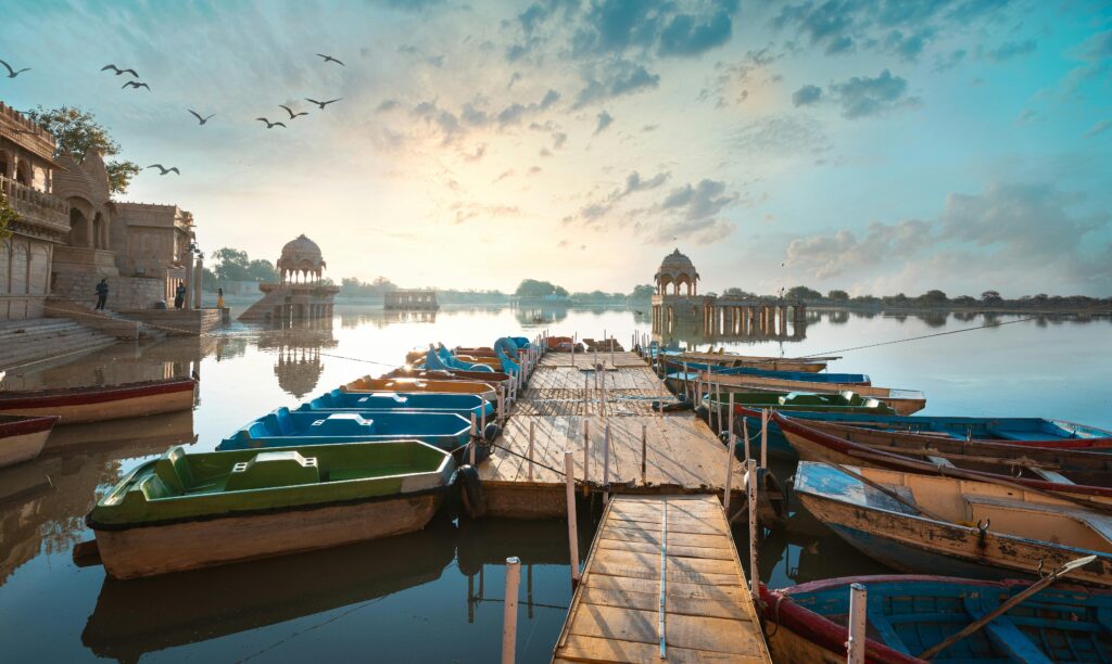 Colorful boats docked at Gadsisar Lake with scenic sunset in Jaisalmer, India.