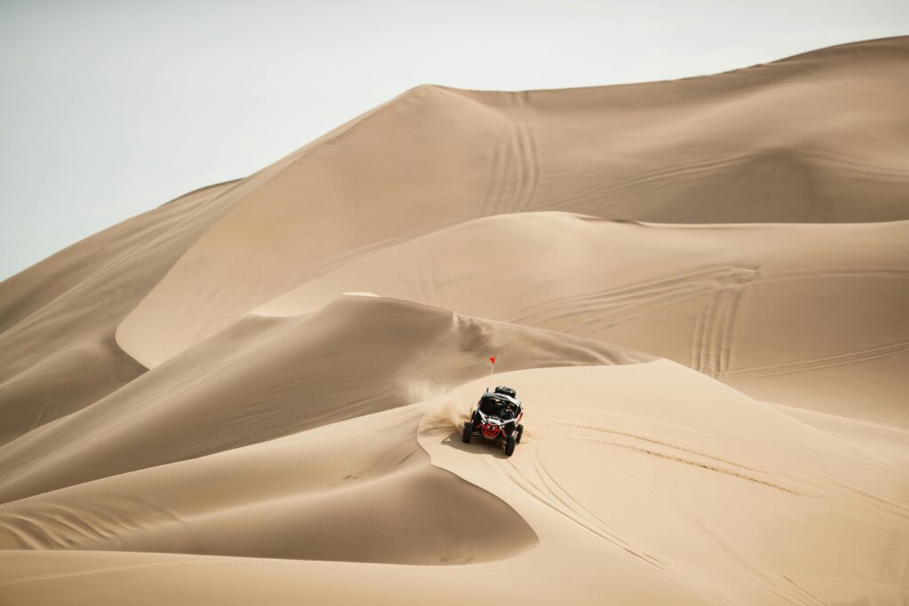 An ATV navigates the vast and sandy desert dunes under bright sunlight.
